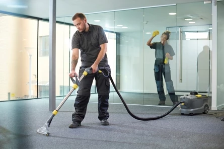 Professionele schoonmaakmedewerkers reinigen grondig het tapijt en glasoppervlakken van een kantoorruimte.
